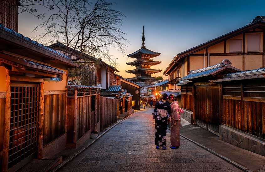Em final de tarde, duas mulheres com quimonos tradicionais, em rua de Kyoto, cidade japonesa para conhecer ao viajar para o japão