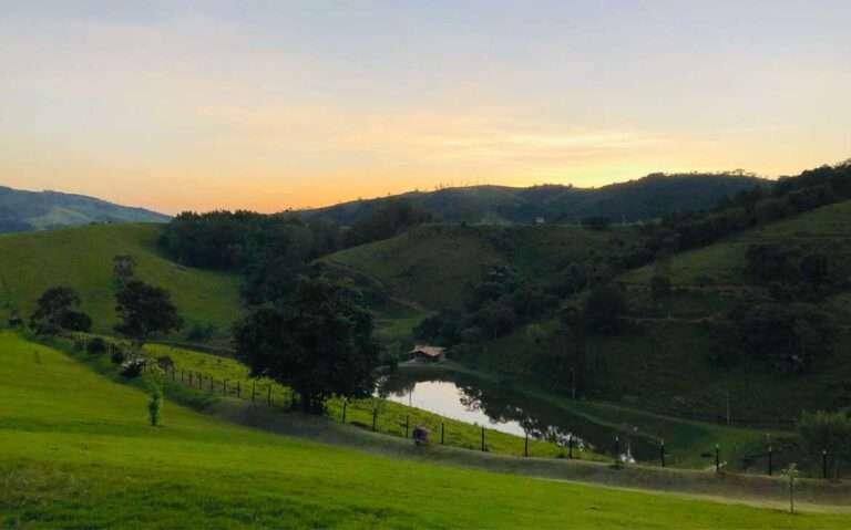 Durante o final de tarde, vista panorâmica de lago cercado por montes e gramados em um dos melhores hotéis fazenda do brasil