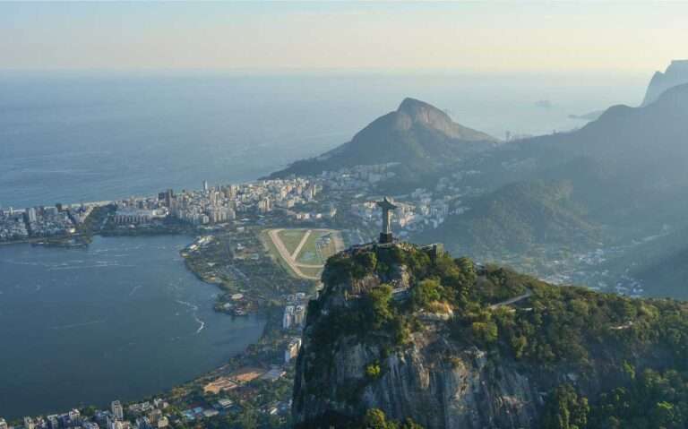 Durante um dia de sol, vista panorâmica e aérea do Rio de Janeiro com o Cristo redentor no centro, e mar árvores, prédios e montanhas ao redor