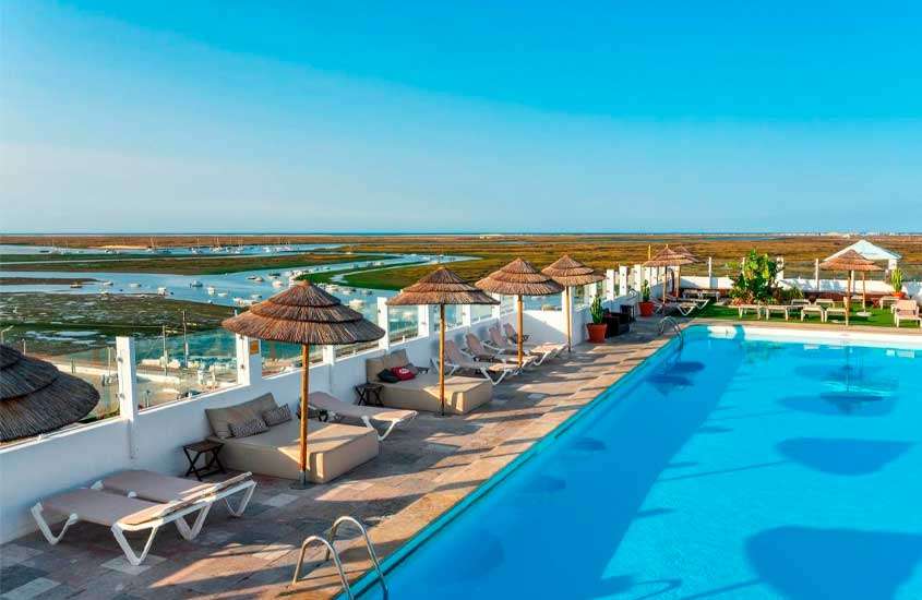 Em dia de sol, cobertura de hotel no Algarve com piscina, espreguiçadeiras, mesas, cadeira e guarda-sóis
