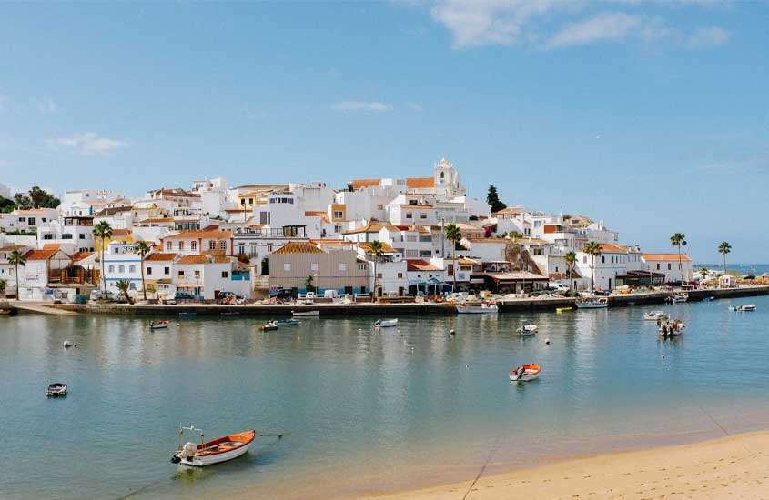 Durante o dia, casas às margens do mar, onde há diversos barquinhos, em Faro, um lugar onde ficar no Algarve