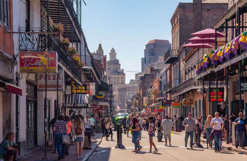 Durante dia de sol, rua de Nova Orleans (cenário de filme A princesa e o sapo) com pessoas, lojas e bandeirinhas penduradas