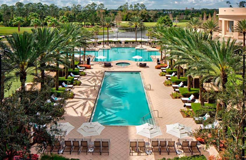 Durante um dia de sol, vista aérea de vista da área de mesas, cadeiras, guarda-sóis e espreguiçadeiras ao redor de duas piscinas em um dos hotéis em Orlando Flórida