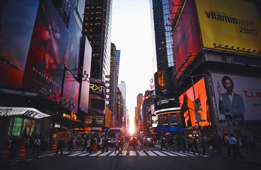 Durante o pôr do sol, rua em Nova Iorque (que foi cenário de filme O diabo veste Prada) com pessoas, banners, telas, carros e cones de trânsito