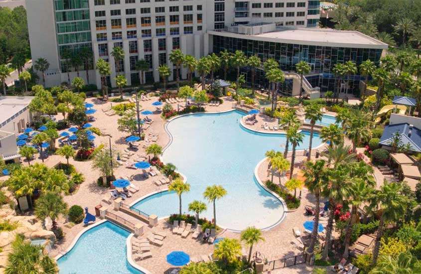 Durante dia e sol, vista aérea de piscina com mesas, cadeiras, espreguiçadeiras, guarda-sóis e prédios de hotel em Orlando ao redor