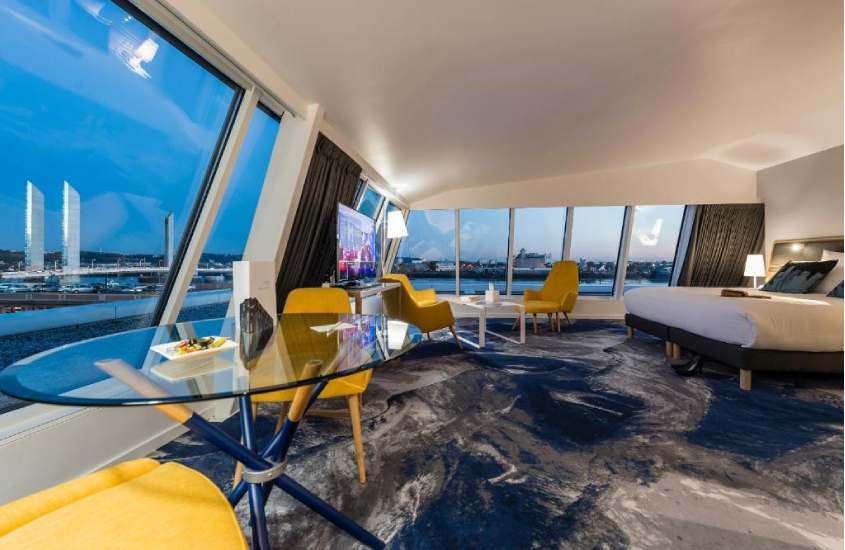 Quarto de hotel em Bordeaux com mesas, cadeiras amarelas, cama de casal, TV, janelas grandes e vista da cidade