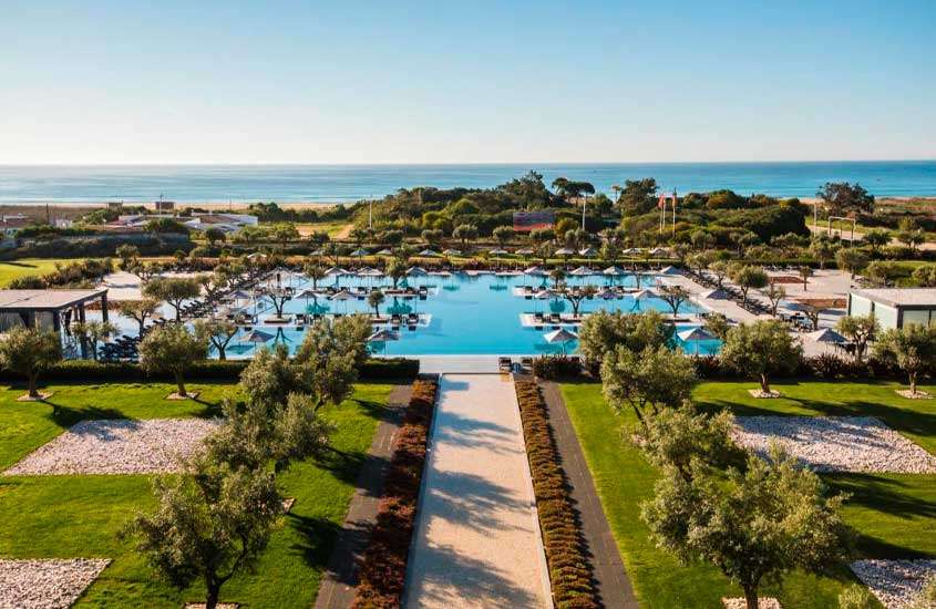 Em dia de sol, vista aérea de árvores e guarda-sóis ao redor de grande piscina ao ar livre em um dos melhores hotéis no Algarve