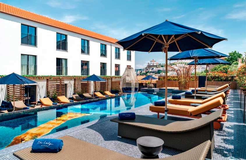 Em dia de sol, espreguiçadeiras com guarda-sóis em frente a grande piscina ao ar livre em um dos melhores hotéis no porto