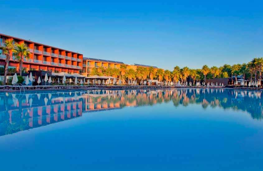 Em final de tarde, espreguiçadeiras e guarda-sóis ao redor de grande piscina ao ar livre em hotel no Algarve