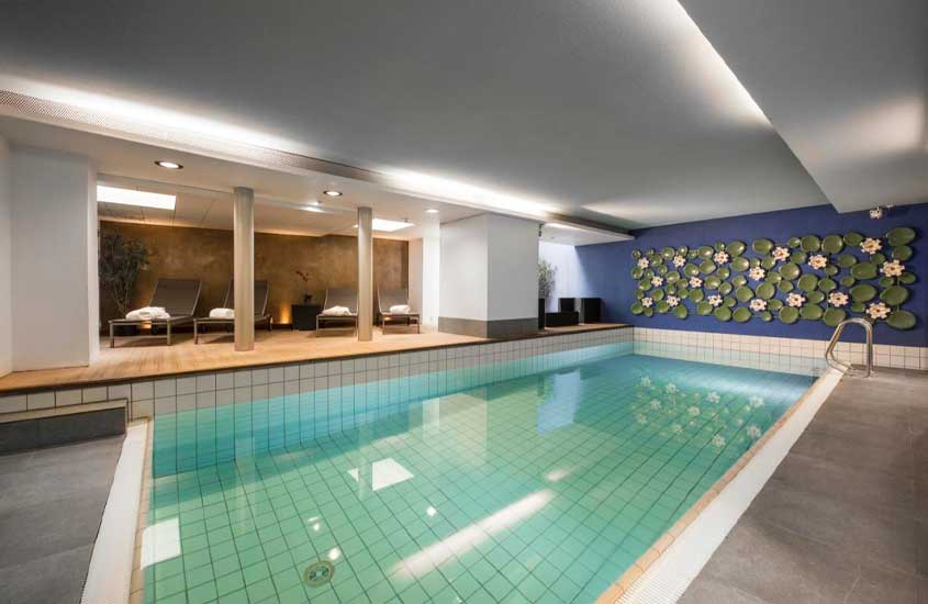 Toalhas de banho em cima de espreguiçadeiras em frente a grande piscina, em área de lazer interna de um dos melhores hotéis em Berna