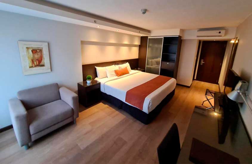 Quarto de hotel onde ficar em Montevideu, com cama de casal, poltrona, armário, estação de trabalho, ar-condicionado, banco de apoio e televisão