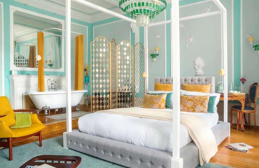 Quarto de hotel no Porto com cama de casal, poltrona, lustre elegante, banheira e mesa com cadeira