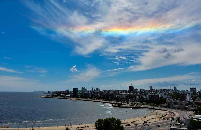Durante dia de sol com arco-íris, vista aérea de prédios às margens do mar