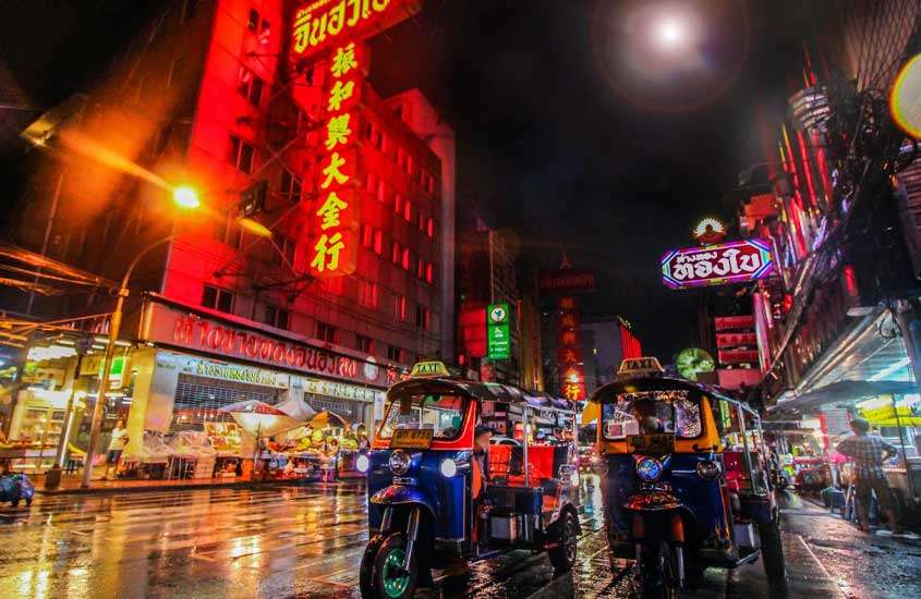 Durante uma noite de chuva, rua de Bangkok cenário de filme ''se beber não case'', com tuktuk, letreiros luminosos, lojas e rua molhada