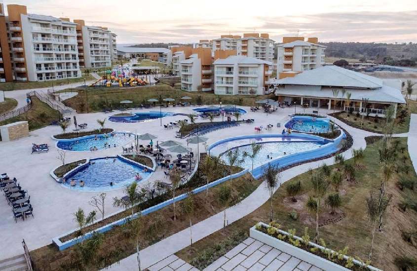 Durante o final da tarde, vista aérea da área de lazer de hotel para lua de mel em caldas novas com piscinas, mesas, cadeiras, espreguiçadeiras, playground e área verde