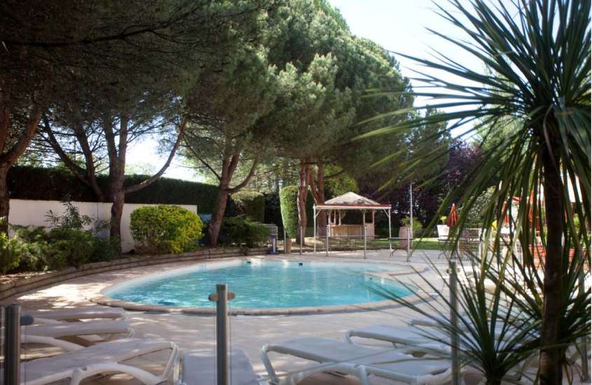 Durante dia de sol, área de lazer de um hotel onde ficar em Bordeaux com piscina, espreguiçadeiras, árvores ao redor, plantas e gazebo