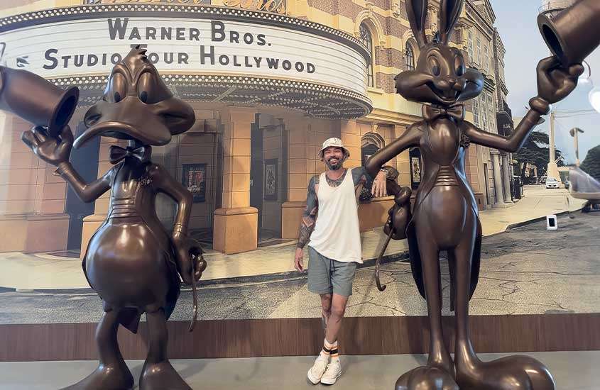 Vagner Alcantelado sorri ao lado das estátuas de Patolino e Pernalonga no Warner Bros. Studio Tour Hollywood, criando um momento divertido e descontraído no passeio.
