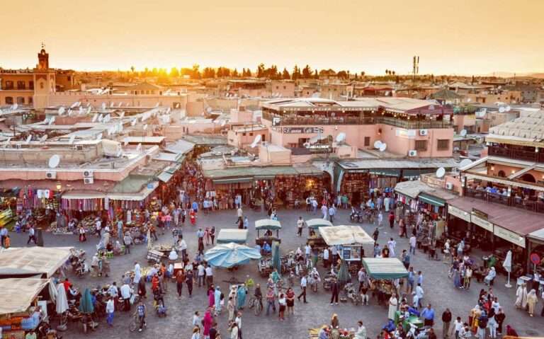 Durante o o pôr do sol, vista aérea de pessoas caminhando em praça repleta de barraquinhas em Marrakech