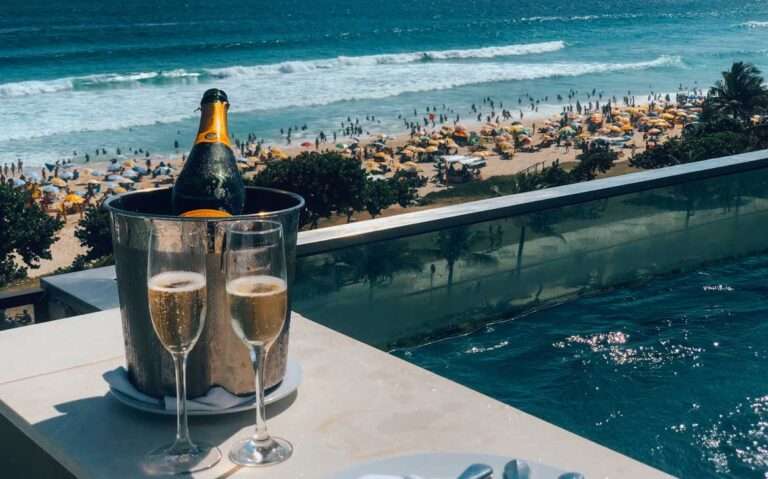 Em dia de sol, balde de champagne em borda de piscina em coberta de hotel com vista para o mar.