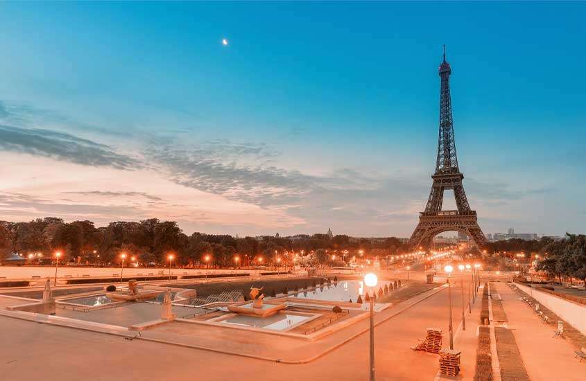Durante o anoitecer vista panorâmica de jardins ao redor da Torre Eiffel, um dos monumentos de uma das cidades da frança com luzes amarelas