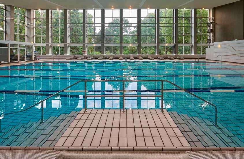 Durante o dia, piscina interna de um hotel em frankfurt com janelas grandes e vista para as árvores