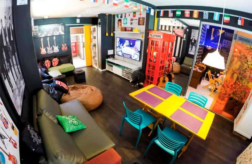 Lounge de hostel com temática de rock, decorado commesas, cadeiras, puffs, TV e luminária