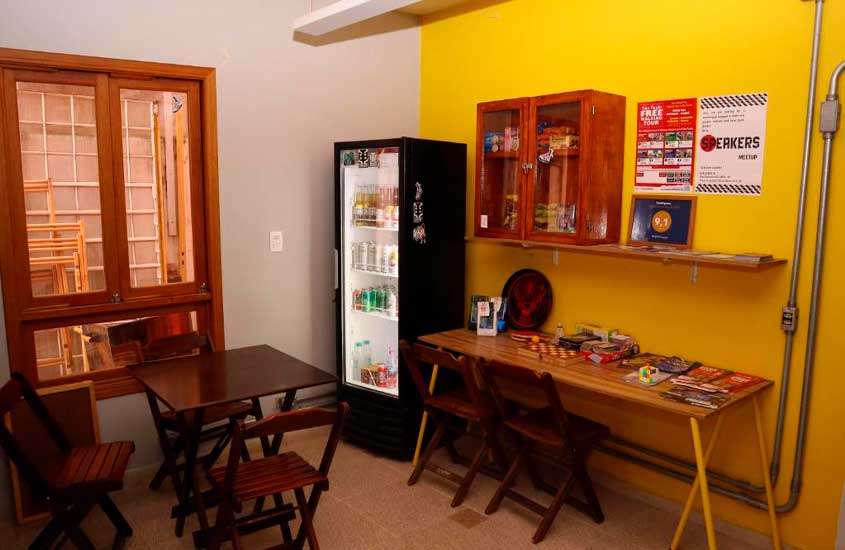 Sala de hoste com mesas, cadeiras, geladeira de bebidas, armário e janelas grandes