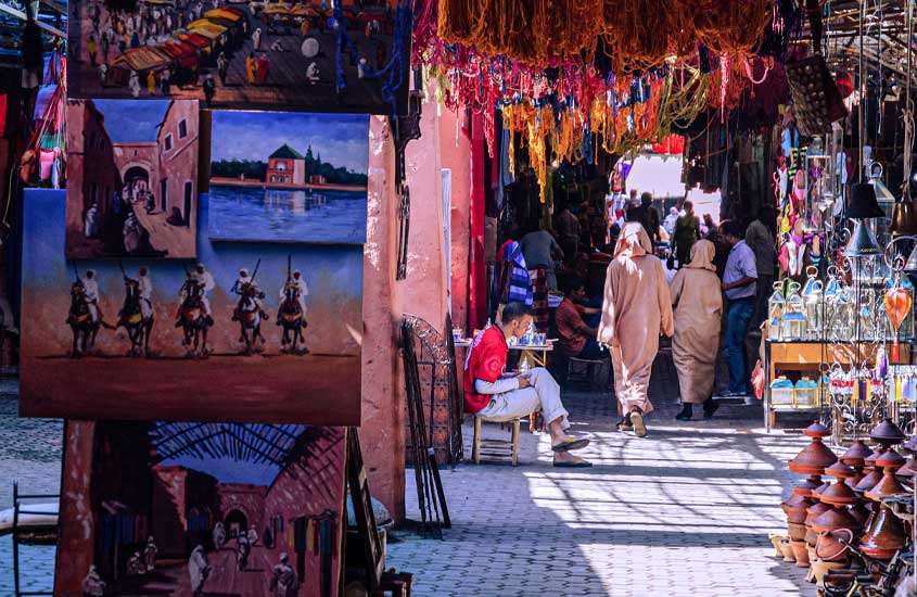 Em dia de sol, interior de um souk com pessoas, pinturas e decorações