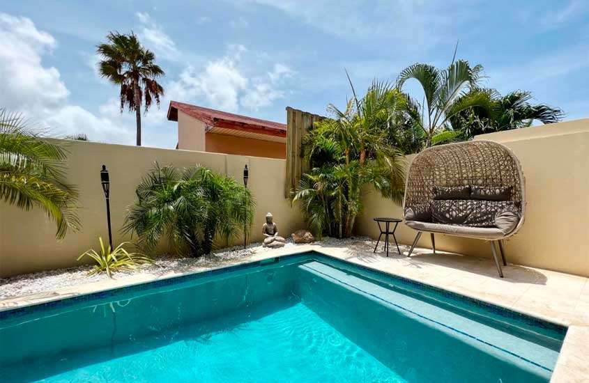 Em um dia de sol, área de lazer de um hotel em aruba com piscina, plantas decorativas e banco acolchoado