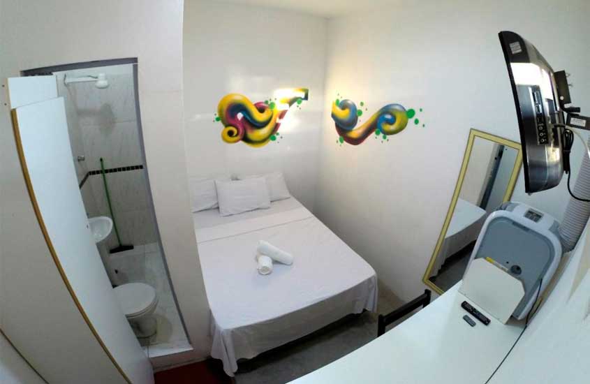 Quarto de hostel com cama de casal, espelho, banheiro, toalhas e tv