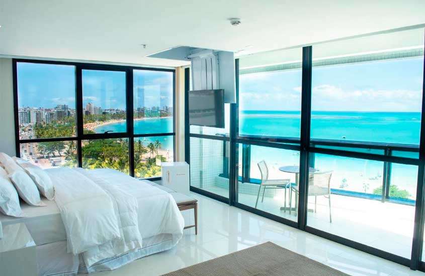 Durante o dia, quarto de um hotéis para lua de mel no brasil com cama de casal, frigobar, varanda, TV, tapete, mesa, cadeiras e horizonte do mar