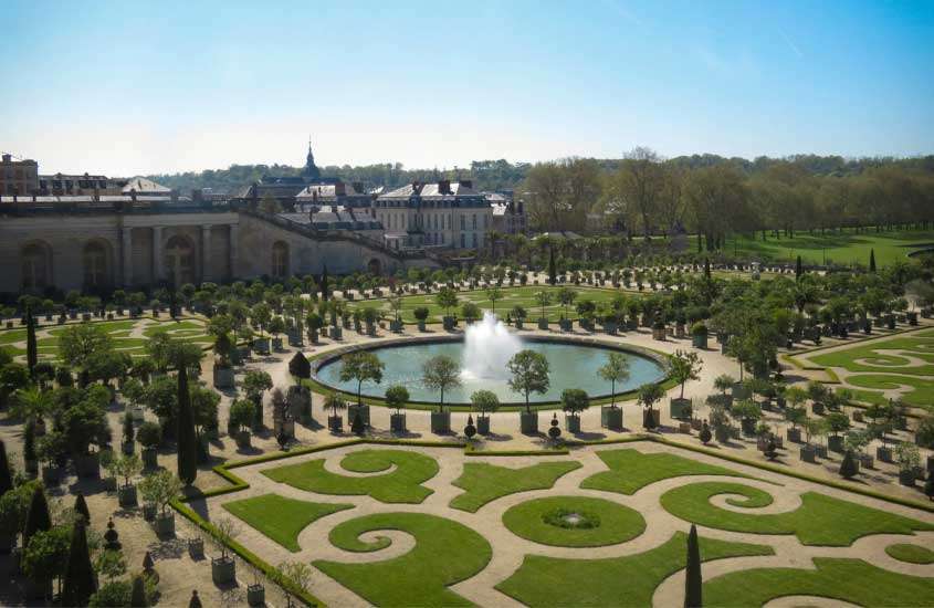 Durante dia de sol, vista aérea dos jardins e do palácios de uma das cidades da frança com chafariz no meio