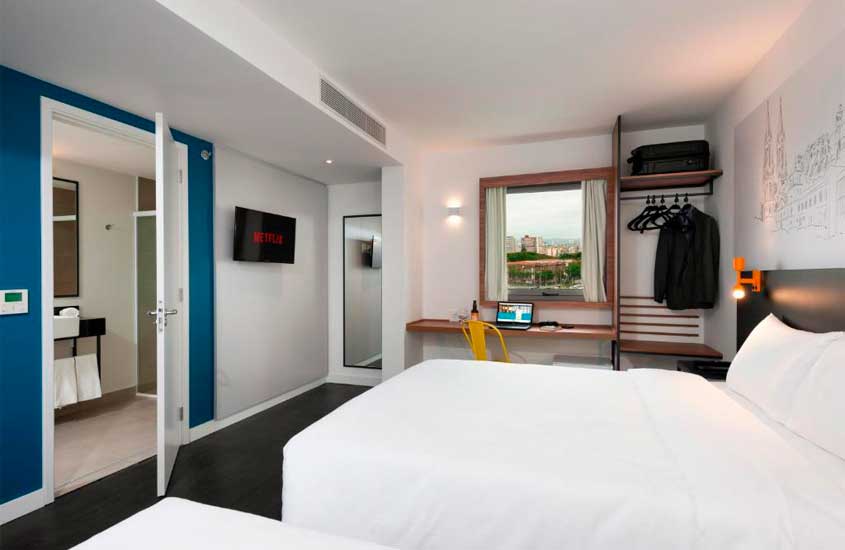 Quarto de hotel pet friendly são paulo com cama de casal, área de trabalho, TV, espelhos, toalhas, armário e janela acortinada
