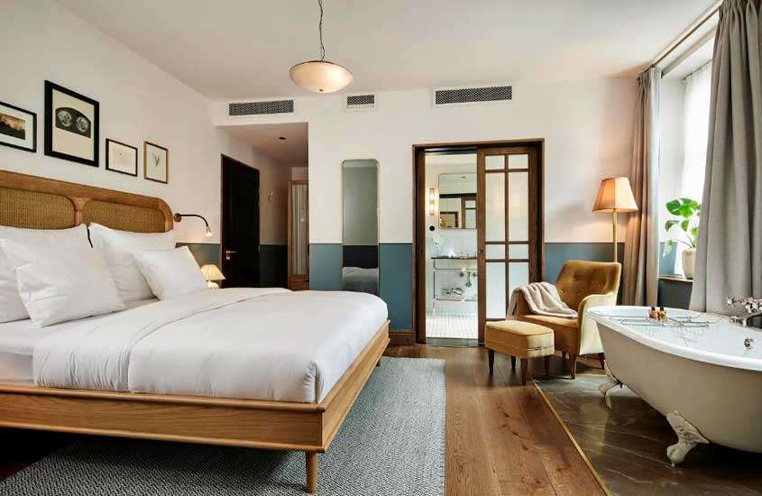 Quarto de hotelem copenhagen com cama de casal, poltrona, banheira, quadros decorativos, luminárias e janela grande acortinada