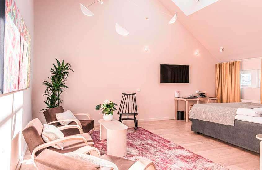 Quarto cor de rosa de um hotel em helsinque com cama de casal, poltronas, mesas, área de trabalho, cadeiras, TV, quadros, janela acortinada e tapete