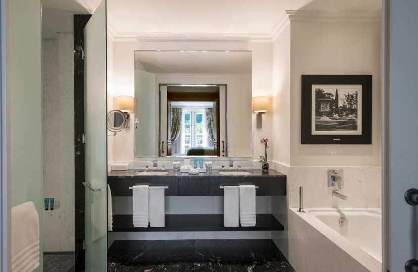 Banheiro de hotel para comemorar aniversário de casamento com duas pias, toalhas, espelhos, luminárias, banheira e quadros decorativos