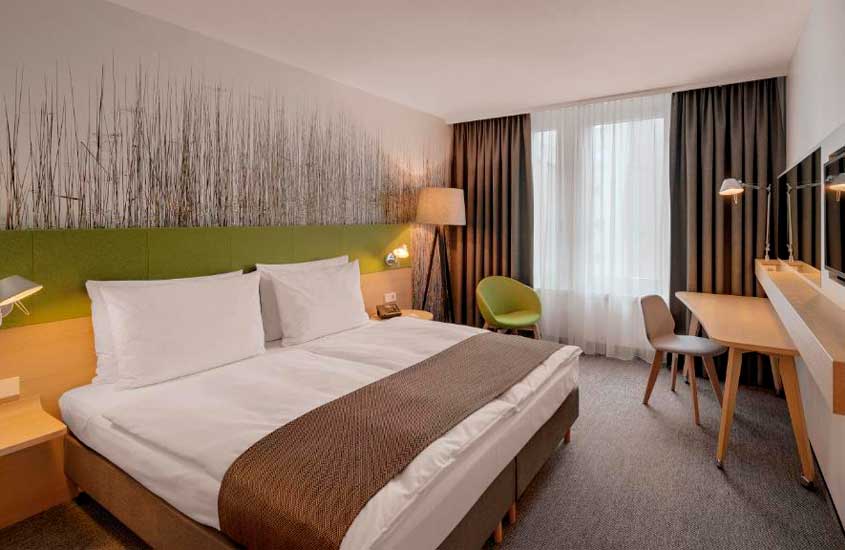 Quarto de hotel em frankfurt com cama de casal, cadeiras, mesa, luminárias, TV e janela acortinada