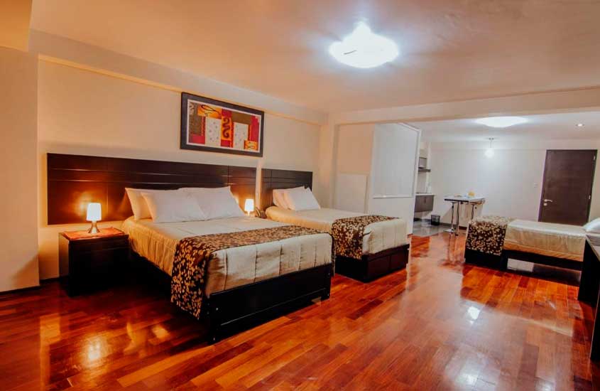 Quarto de hotel onde se hospedar em cusco com camas de casal, piso de madeira, quadro decorativo, minicozinha e armário