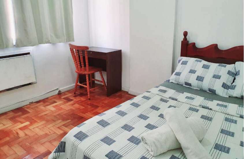 Quarto de hostel em copacabana rio de janeiro com cama de casal, cadeira, mesa, janela acortinada e piso da madeira