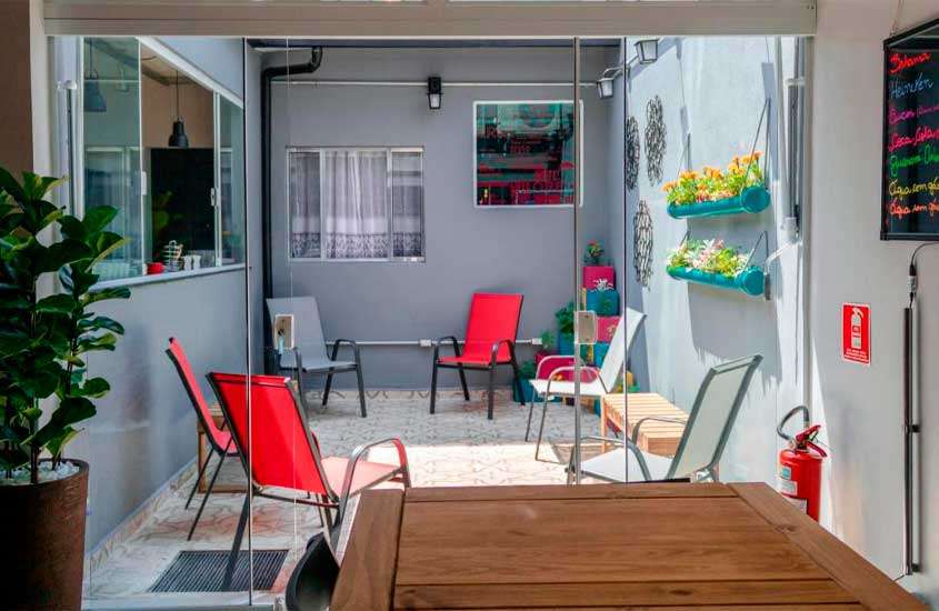 Lounge de hostel em são paulo com mesa, cadeiras, flores decorativas e janelas grandes
