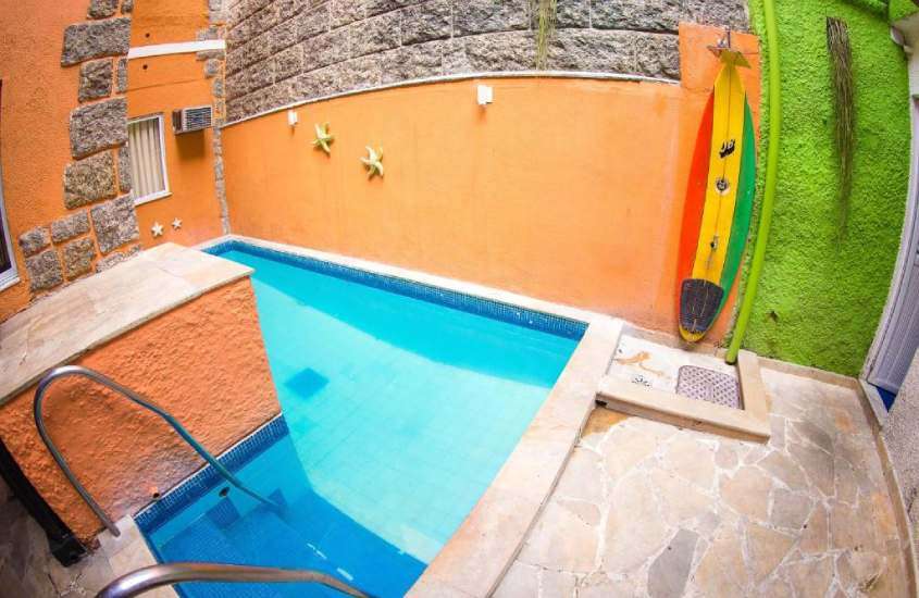 Em um dia de sol, área de lazer de um dos melhores hostels em copacabana com piscina, prancha decorativa e parede de pedra