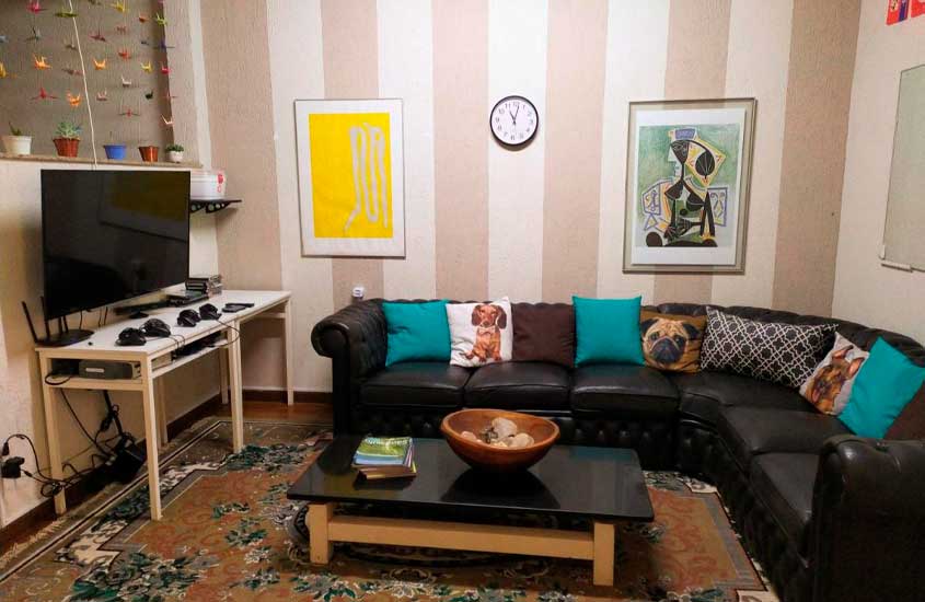 Sala de hostel em são paulo, com mesas, sofá, TV, relógio, tapete e quadros decorativos