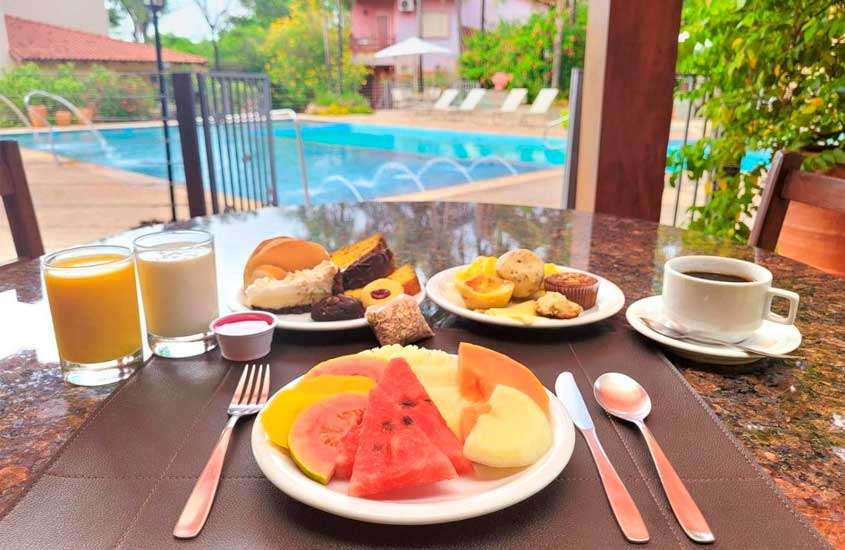 Durante o dia, café da manhã com frutas, pães e sucos, servido em mesa com vista para a piscina