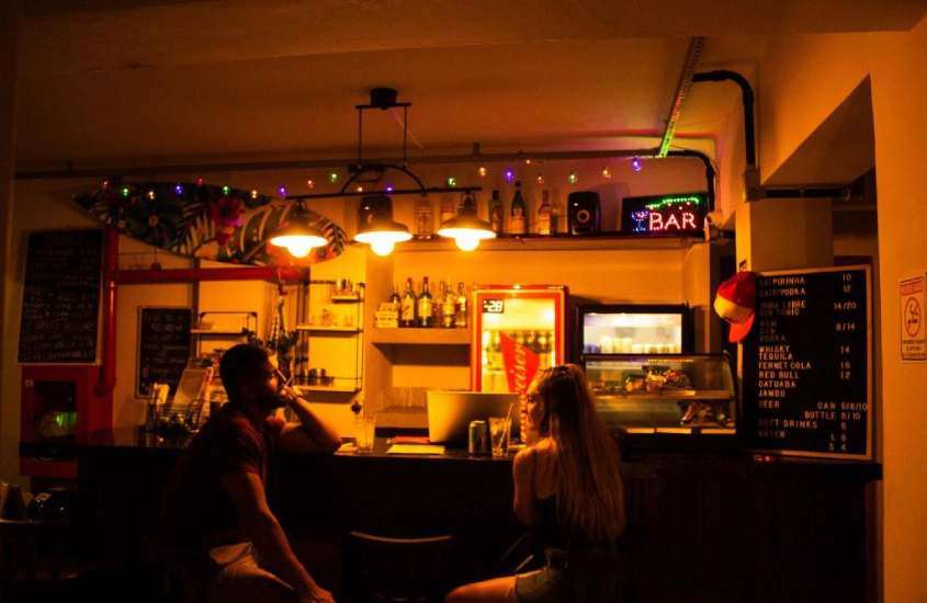 Bar de um hostel em copacabana com pessoas, cadeiras, bebidas e geladeira