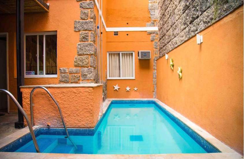 Em um dia de sol, área de lazer de hostel em copacabana com piscina, estrelas decorativas e paredes de pedra