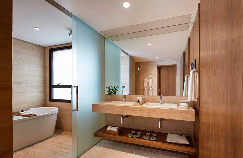Banheiro de um hotel para comemorar aniversário de casamento com banheira, 2 pias, toalhas, chinelos, roupões, espelho e janela lateral