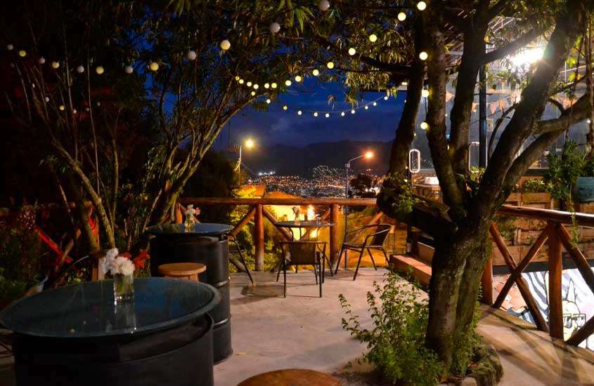 Durante a noite, cobertura de um hotel onde se hospedar em cusco com mesa, cadeiras, bancos, luzinhas, árvores e plantas decorativas