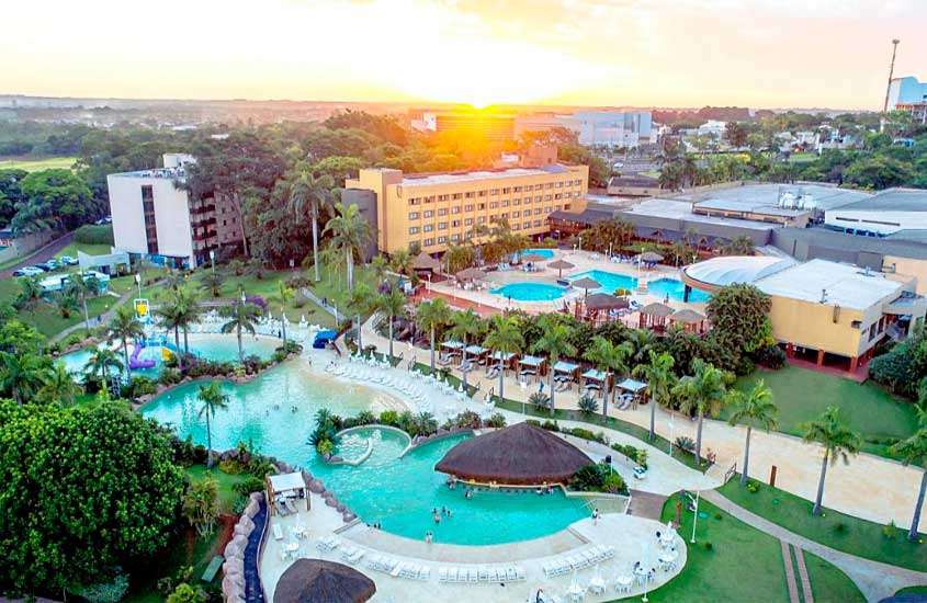 Durante o põr do sol, vista panorâmica de um dos hotéis onde ficar em foz do iguaçu com piscinas, mesas, cadeiras, espreguiçadeiras e árvores