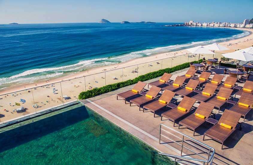 Durante dia de sol, um dos hotéis que aceitam pet no Rio de Janeiro com vista para a praia, espreguiçadeiras com toalha e piscina de borda infinita