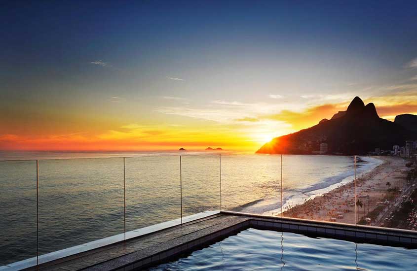 Durante o pôr do sol, área de lazer de hotel com piscina e vista para o mar